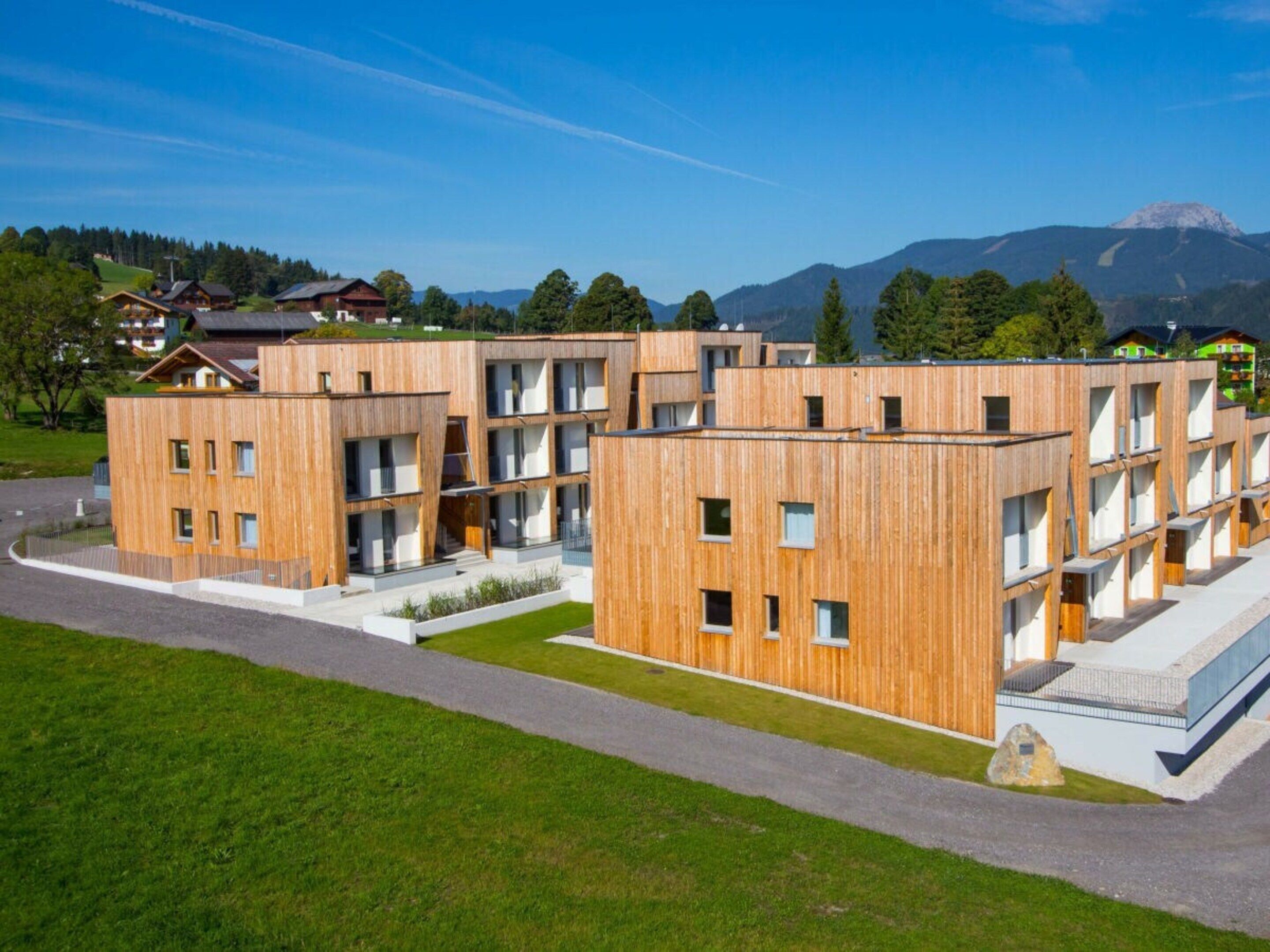 A modern multi-story building with a wooden facade, multiple balconies, and a paved driveway.