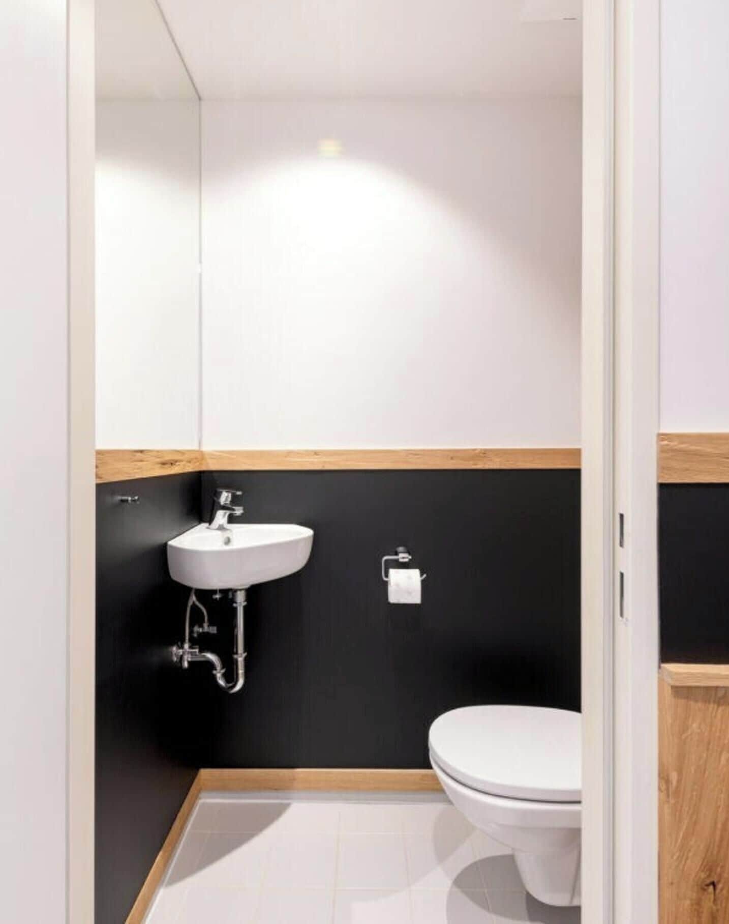Un baño moderno con lavamanos blanco, pared negra y detalles de madera.