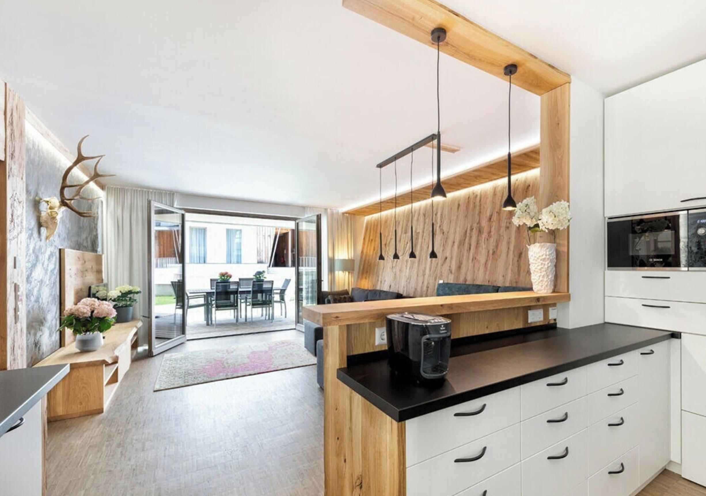 Una cocina moderna con encimera de madera, armarios blancos y un comedor con puerta de vidrio que da al exterior.