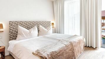 A hotel room with a large bed, a headboard with a patterned design, two bedside lamps, and a view of a balcony with curtains.