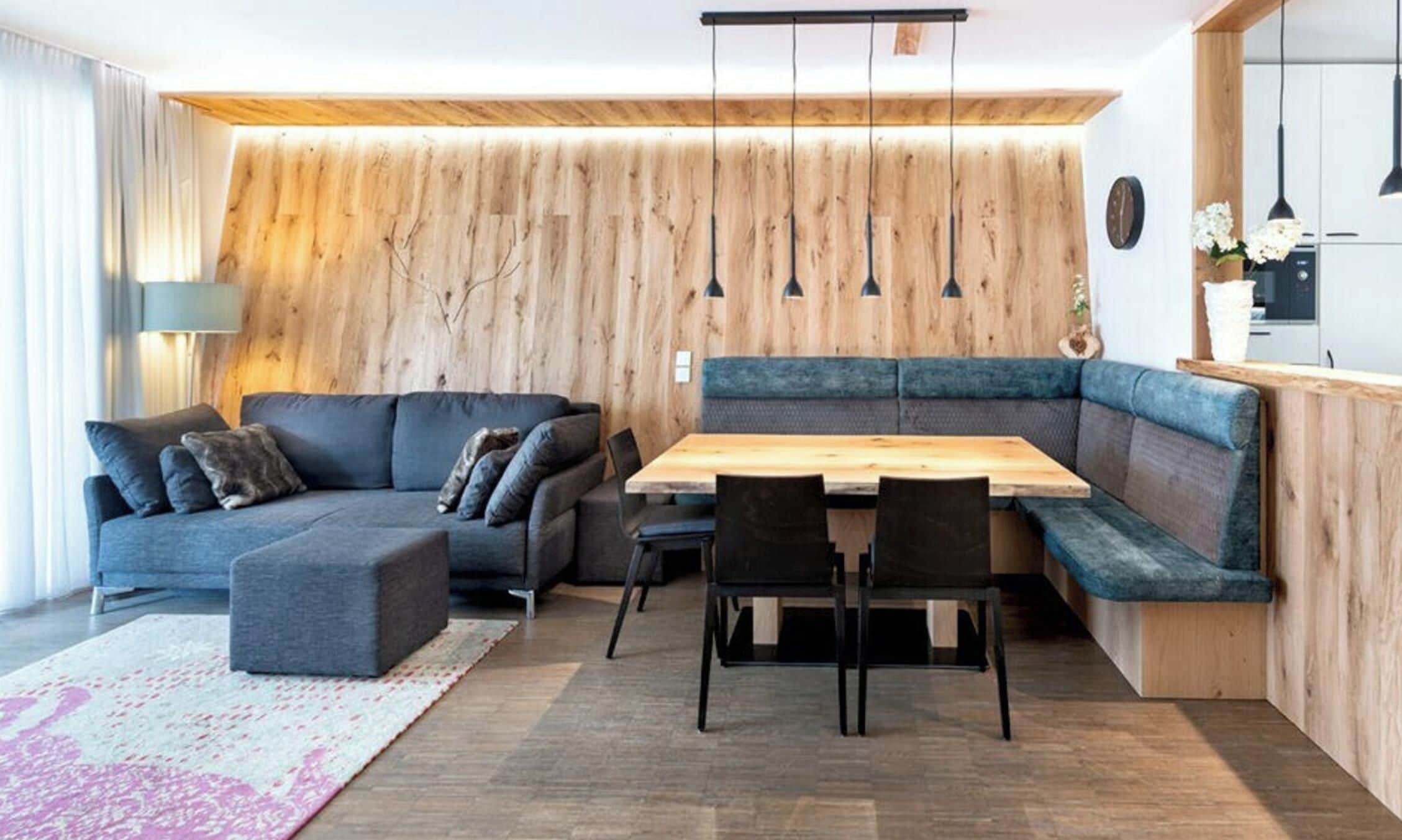 Ein stilvoller Wohnraum mit einer Wandpaneele aus Holz, einem grauen Sofa, einem Holztisch und schwarzen Stühlen.