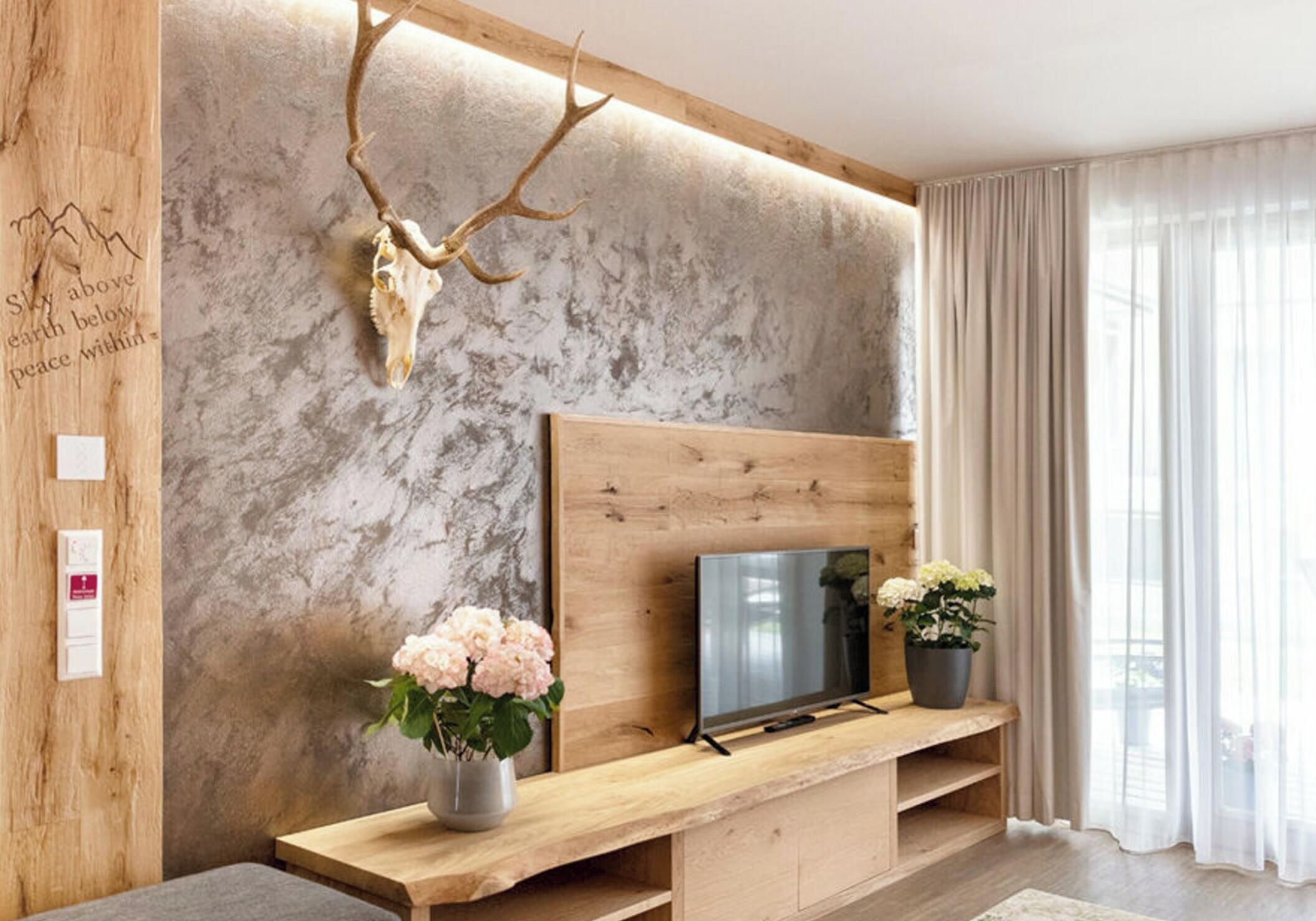 Una sala moderna con un mueble de madera para entretenimiento, un televisor montado y una cornamenta decorativa.