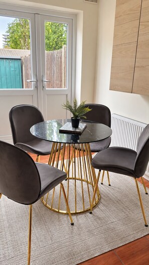 A dining area with a round table, four chairs, a potted plant, and a view of the outside. - Spacious 4-bed Southall | Free Parking | Sleeps 9 (Southall)