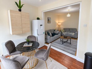 A modern living room with a grey sofa, a dining area with a marble table, and a white refrigerator. - Spacious 4-bed Southall | Free Parking | Sleeps 9 (Southall)