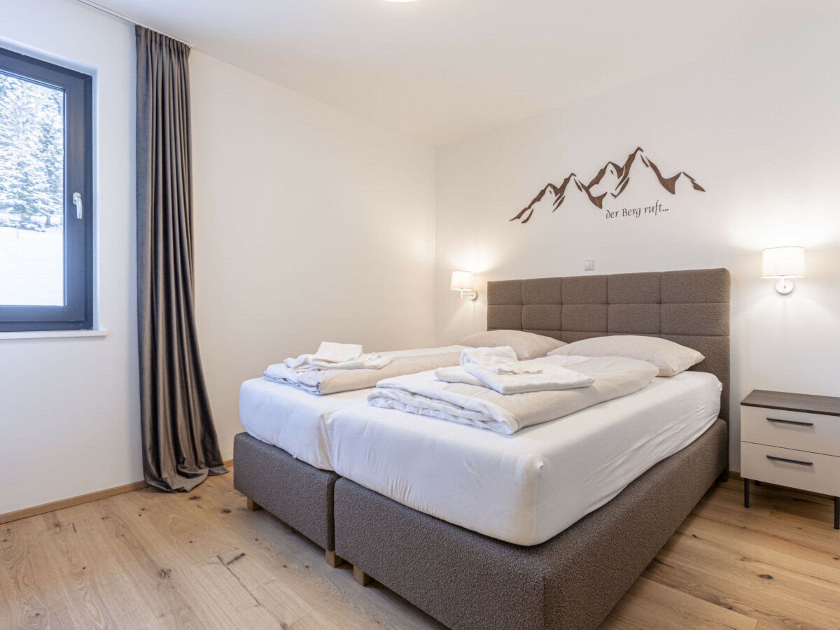 A bedroom with a bed, two bedside tables, a window with curtains, and a wall decoration.