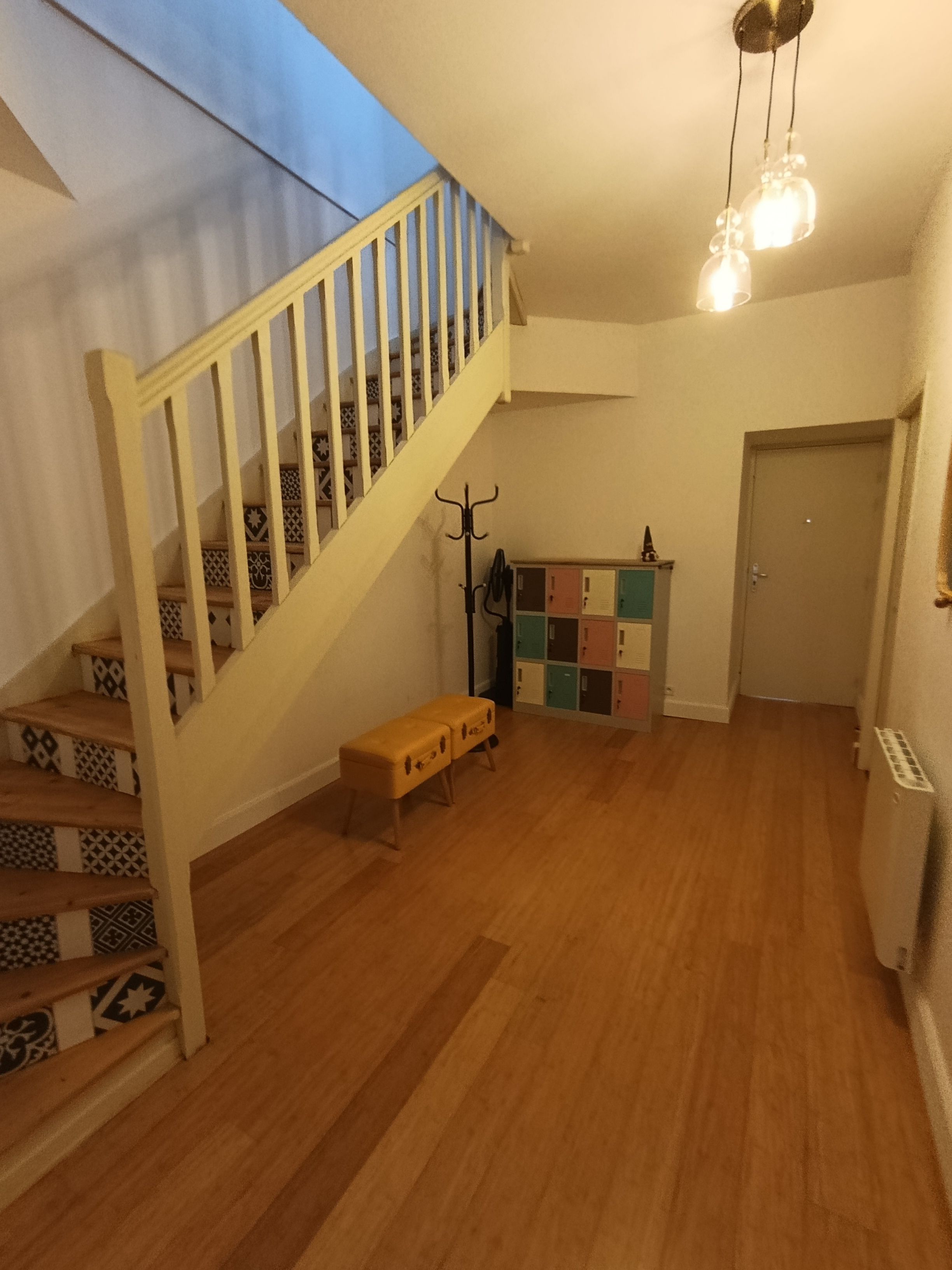 Un escalier avec des marches décorées menant à un palier, un banc, un porte-manteau et une rangée de casiers.