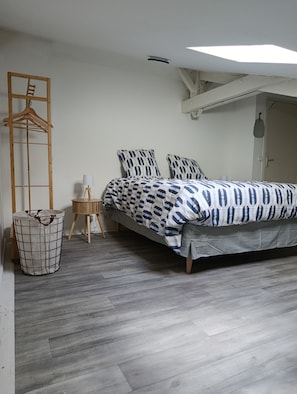 A bedroom with a bed, a wooden hanger, a lamp, a waste basket, and a ceiling light. - The Carmel Tour. A unique apartment in the heart of Fontenay-le-Comte. (Fontenay-le-Comte)