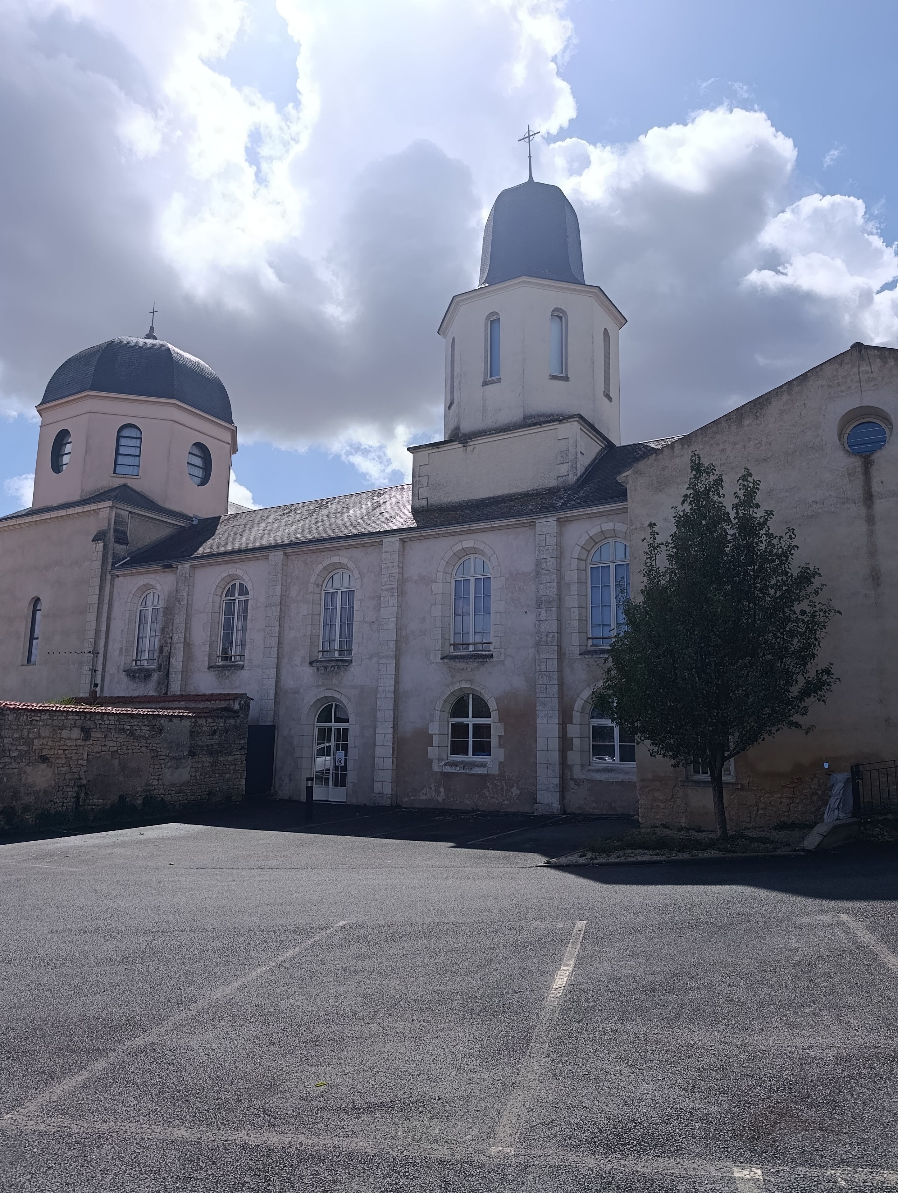 Un bâtiment doté d’un dôme et d’un clocher, une zone pavée devant et un arbre.