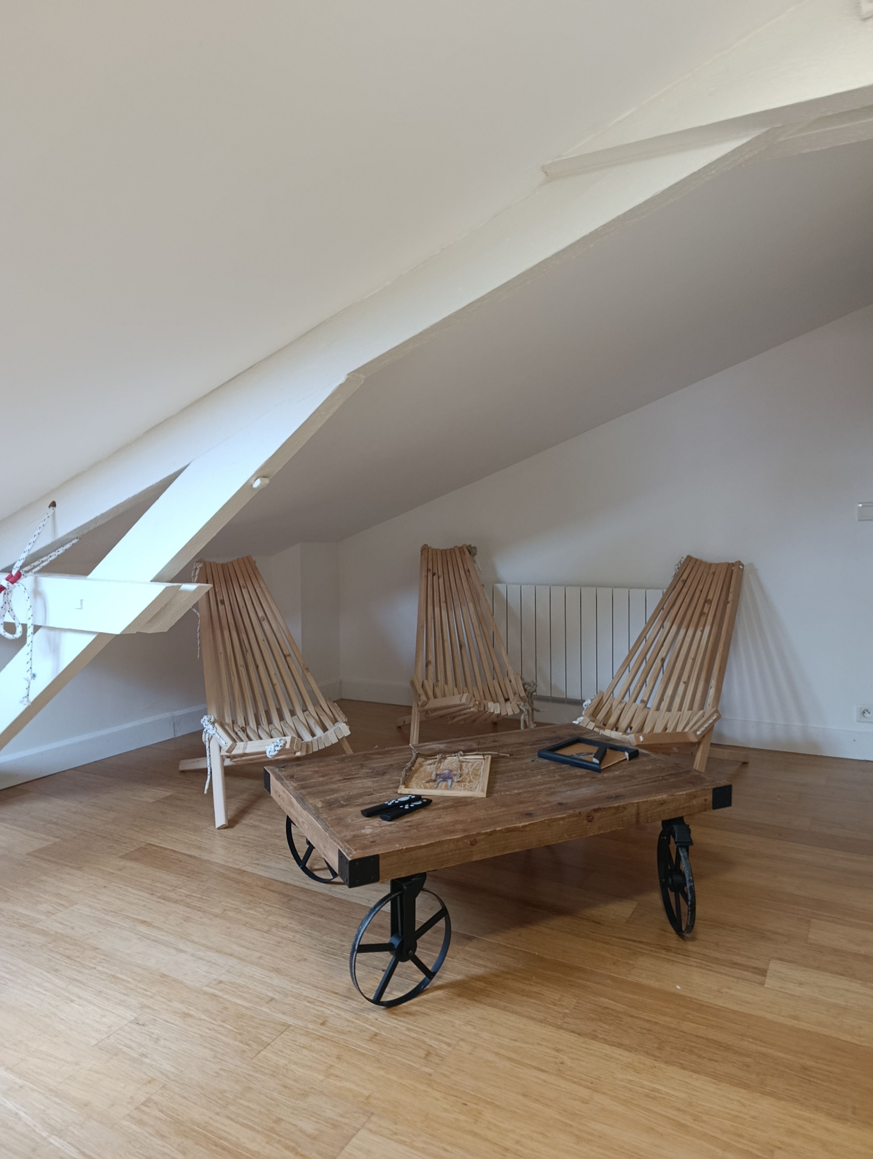 Een kamer met een schuine kap, een houten tafel met stoelen en een radiator aan de muur.