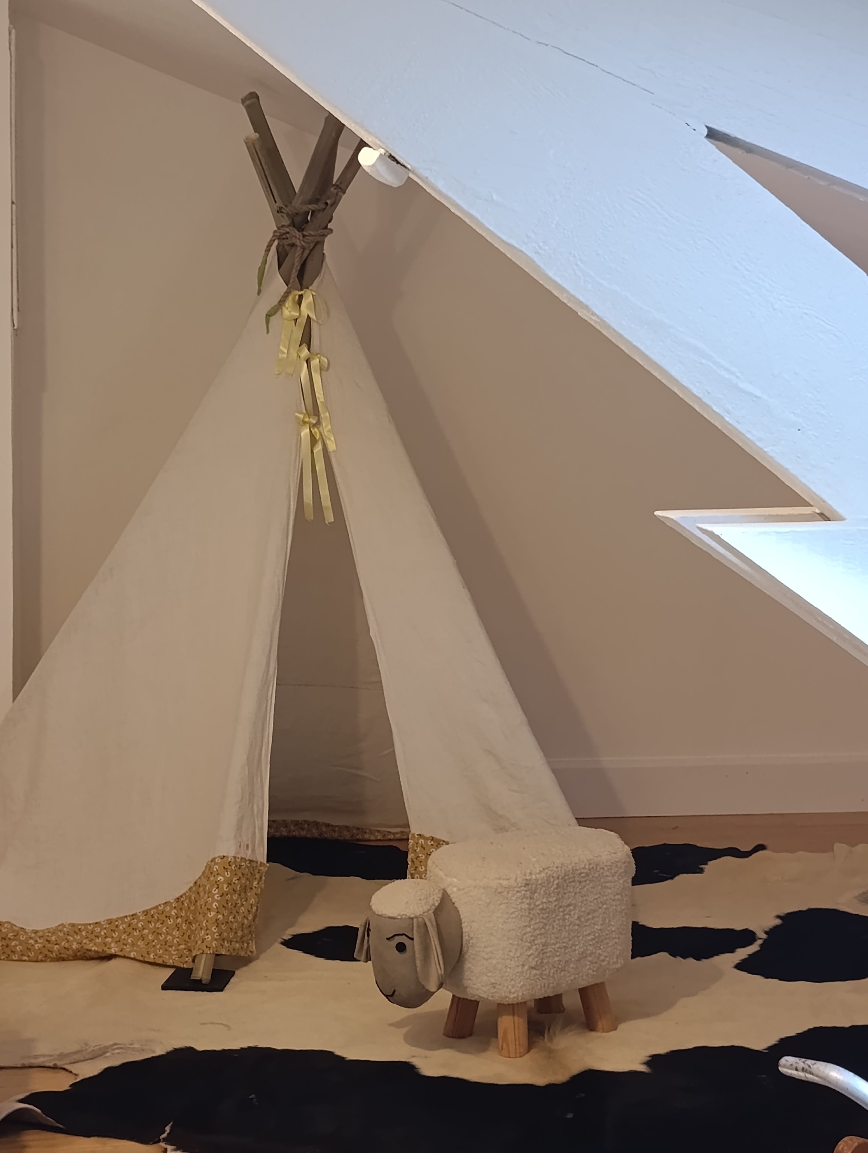 Een tentvormige constructie met een houten frame en een witte stoffen ingang.