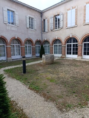 A courtyard with a gravel path, a stone planter, and a building with arched windows and brickwork.