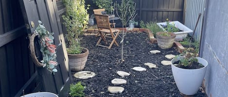 Un sendero en un jardín con piedras para pisar, rodeado de plantas en macetas y una silla de madera.