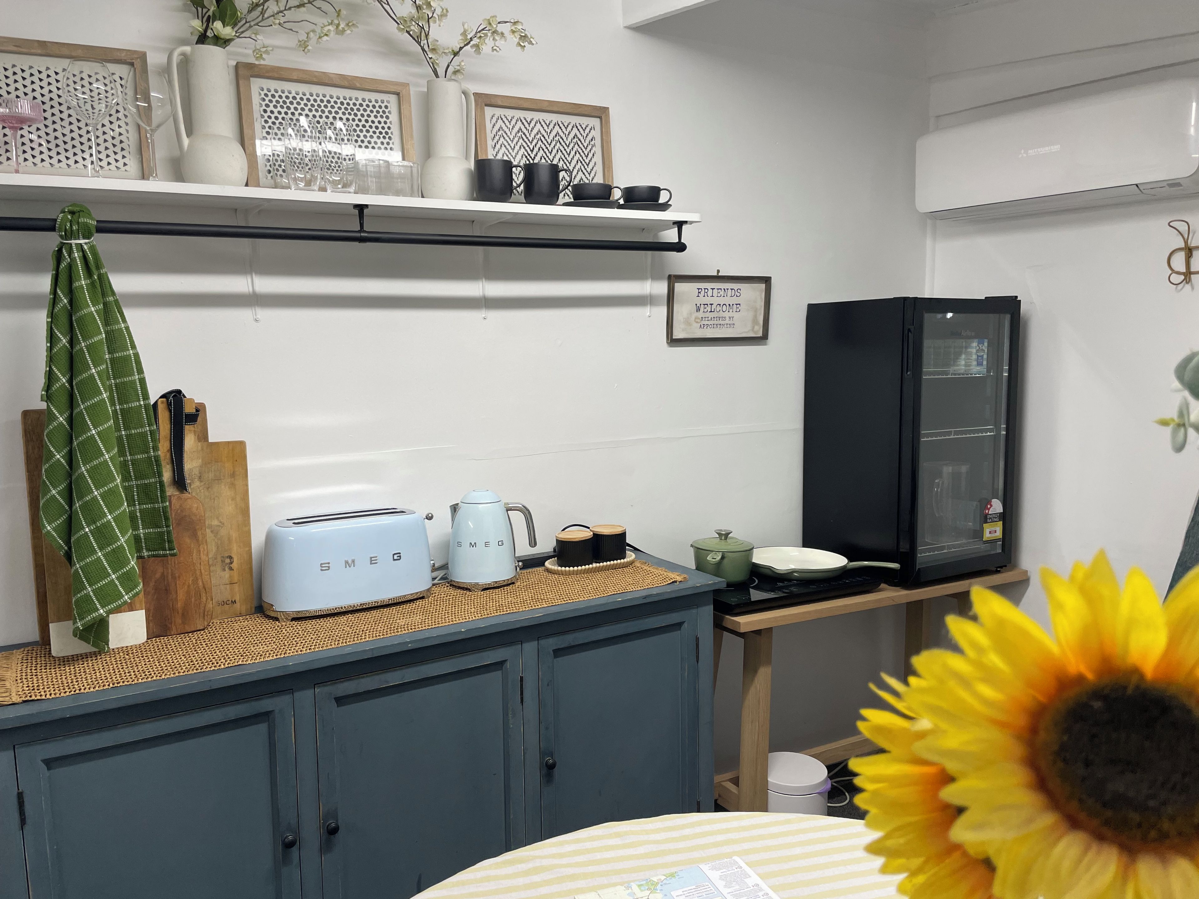 Eine Küche mit einer Arbeitsplatte, einem Toaster, einem Wasserkocher, einem Kühlschrank und einem an der Wand befestigten Regal mit Dekorationen.