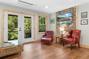 A room with a stone wall, two windows, a fireplace, a television, and two leather chairs. - Blackberry Woods | A Peaceful Maine Retreat in Hope (Hope)