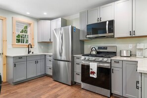 A modern kitchen with stainless steel appliances, grey cabinets, and a wooden floor. - Blackberry Woods | A Peaceful Maine Retreat in Hope (Hope)