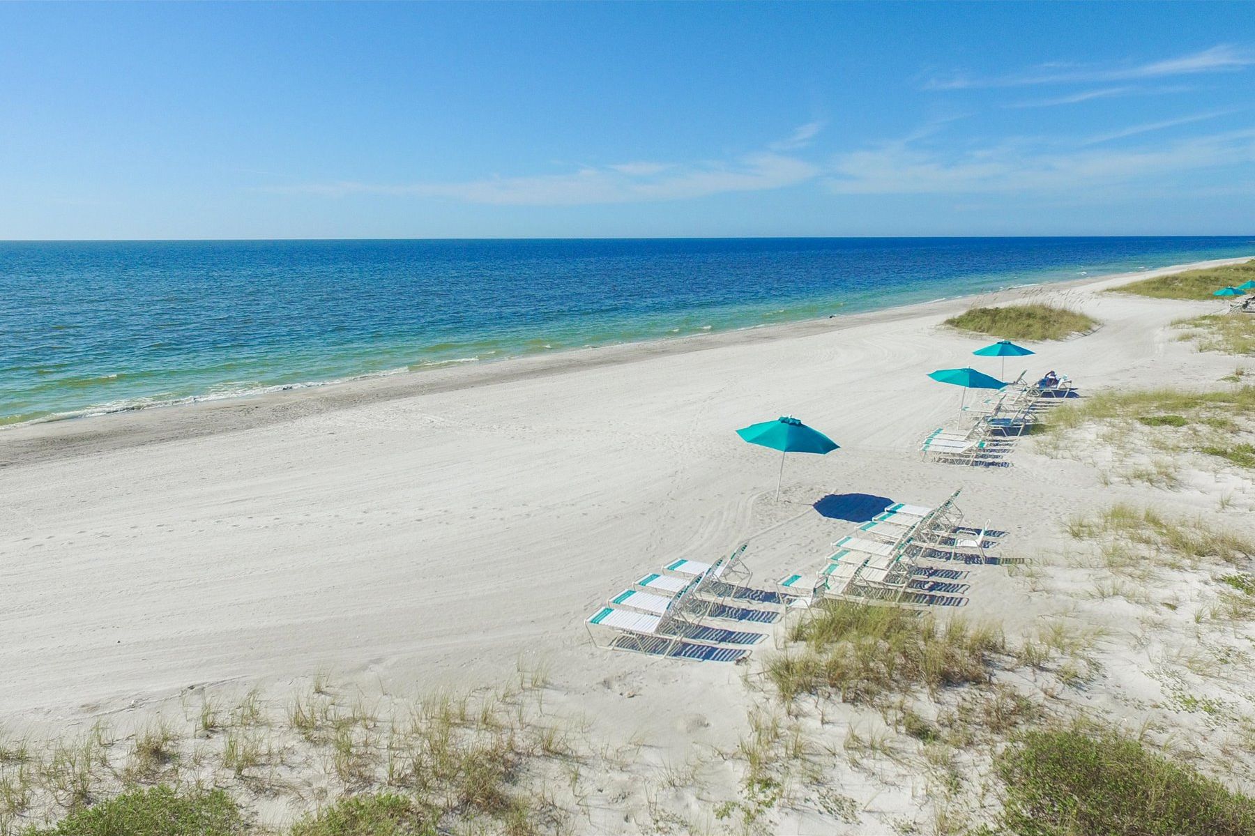 Ein Strand mit Liegestühlen und Sonnenschirmen, ein klarer Himmel und das Meer im Hintergrund.