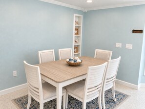 A dining area with a light blue wall, a wooden table, white upholstered chairs, and a basket of decorative items on the table. - 3/2.5 Canal Front Home, Private Pool, Dock on LBK (Longboat Key)