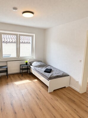 A small, single-bed room with a window, a radiator, a desk, and a chair. - Copy of Worker and holiday apartment Lingenfeld (Lingenfeld)