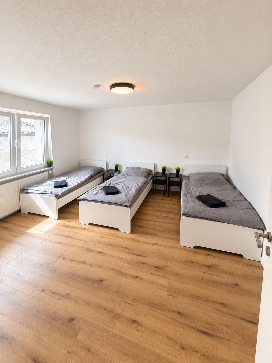 Ein Zimmer mit drei Einzelbetten, einem Fenster und einer Heizung.