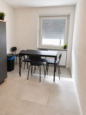 Ein kleiner Essbereich mit Tisch und Stühlen, einem Heizkörper und einem Fenster mit Jalousien.