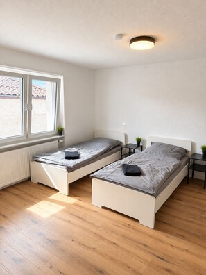 Un dormitorio con dos camas individuales, una ventana, un radiador y una lámpara en el techo.