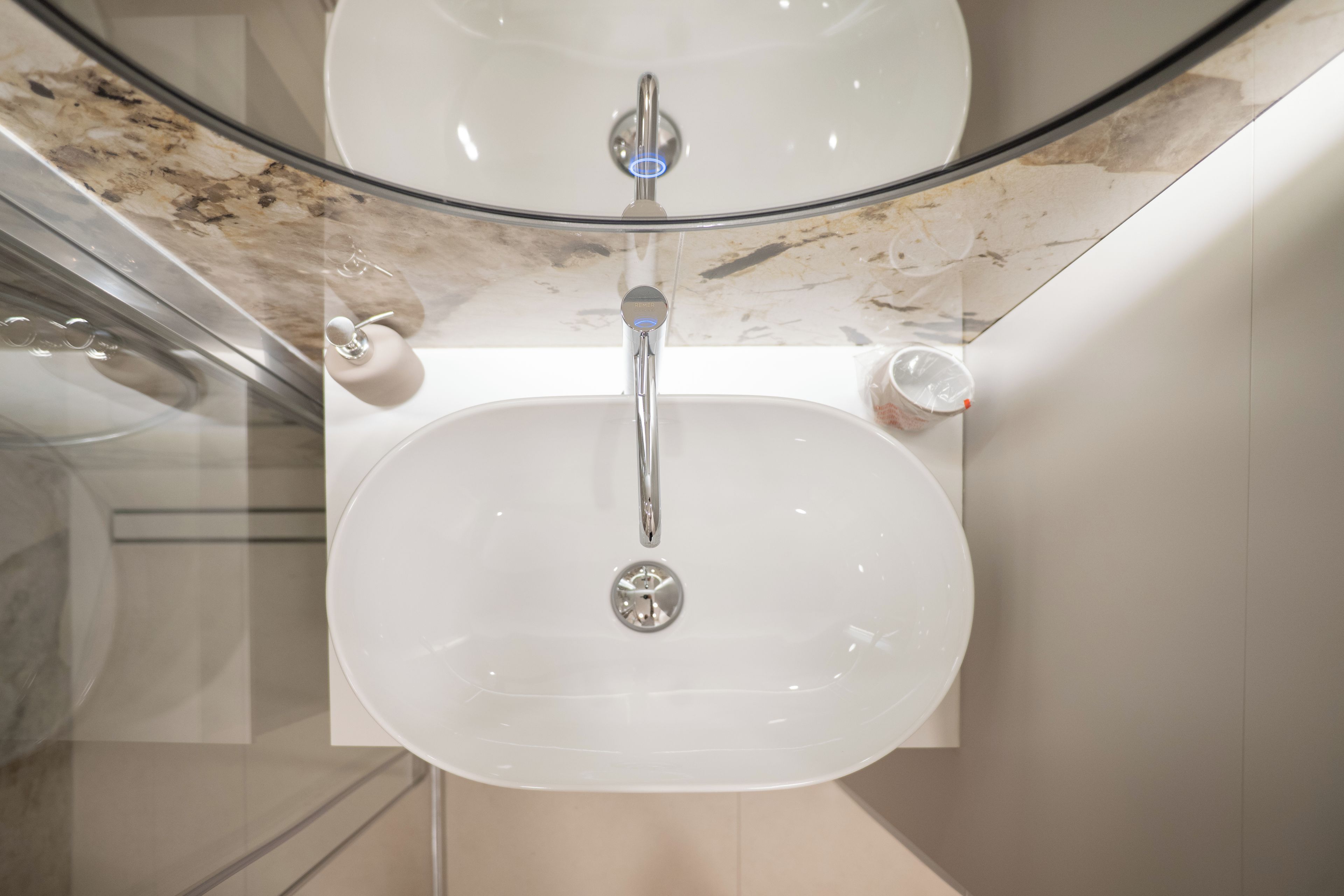 Une salle de bain avec un lavabo blanc, un miroir et une paroi de douche en verre.