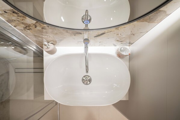 Un baño con un lavamanos blanco, un espejo y una cabina de vidrio.