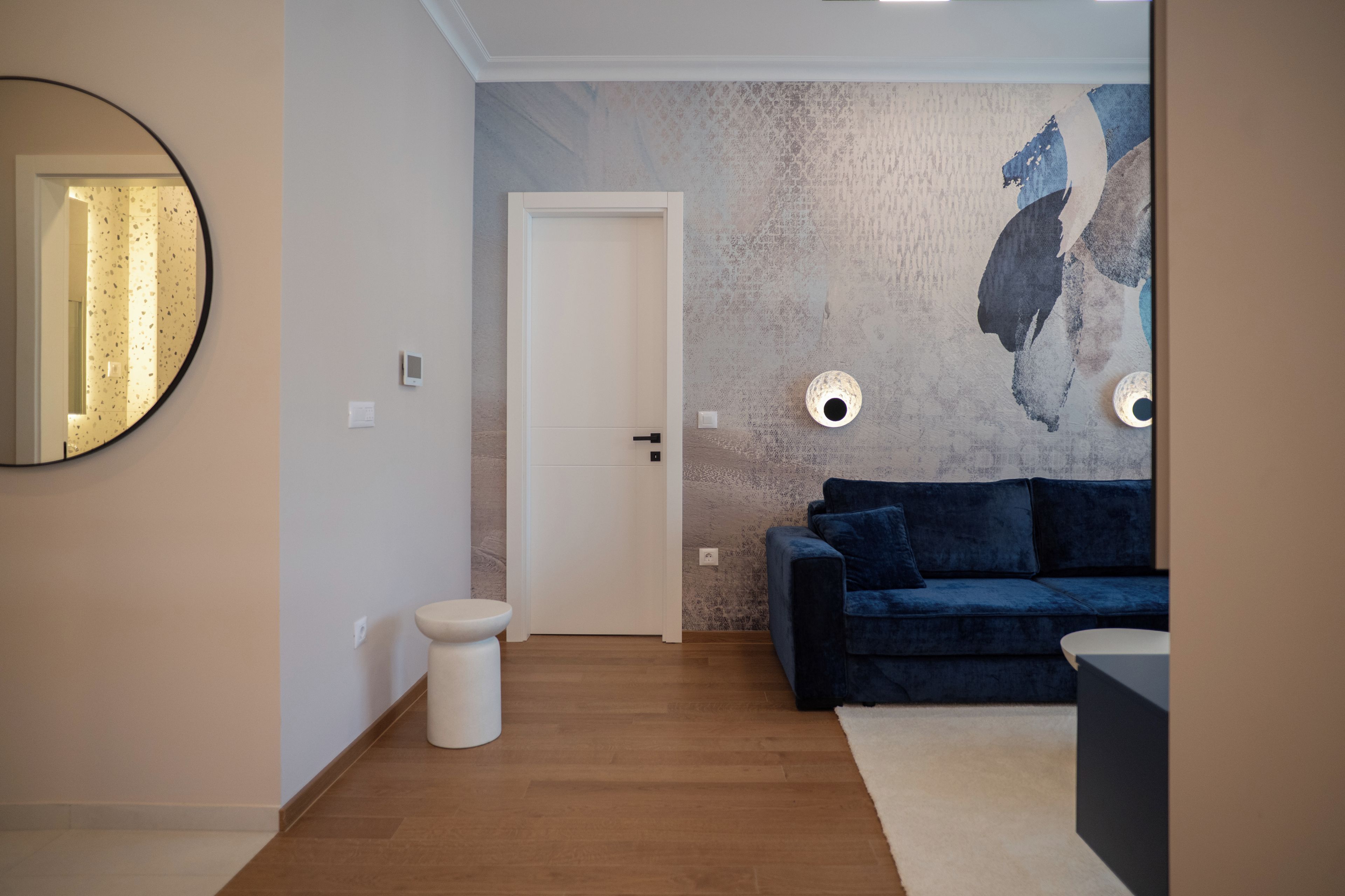 A modern living room with a blue sofa, a round mirror, and a textured wall.