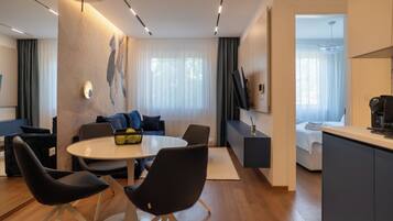 Una habitación de hotel moderna con zona de comedor, sofá, televisión y cocina.