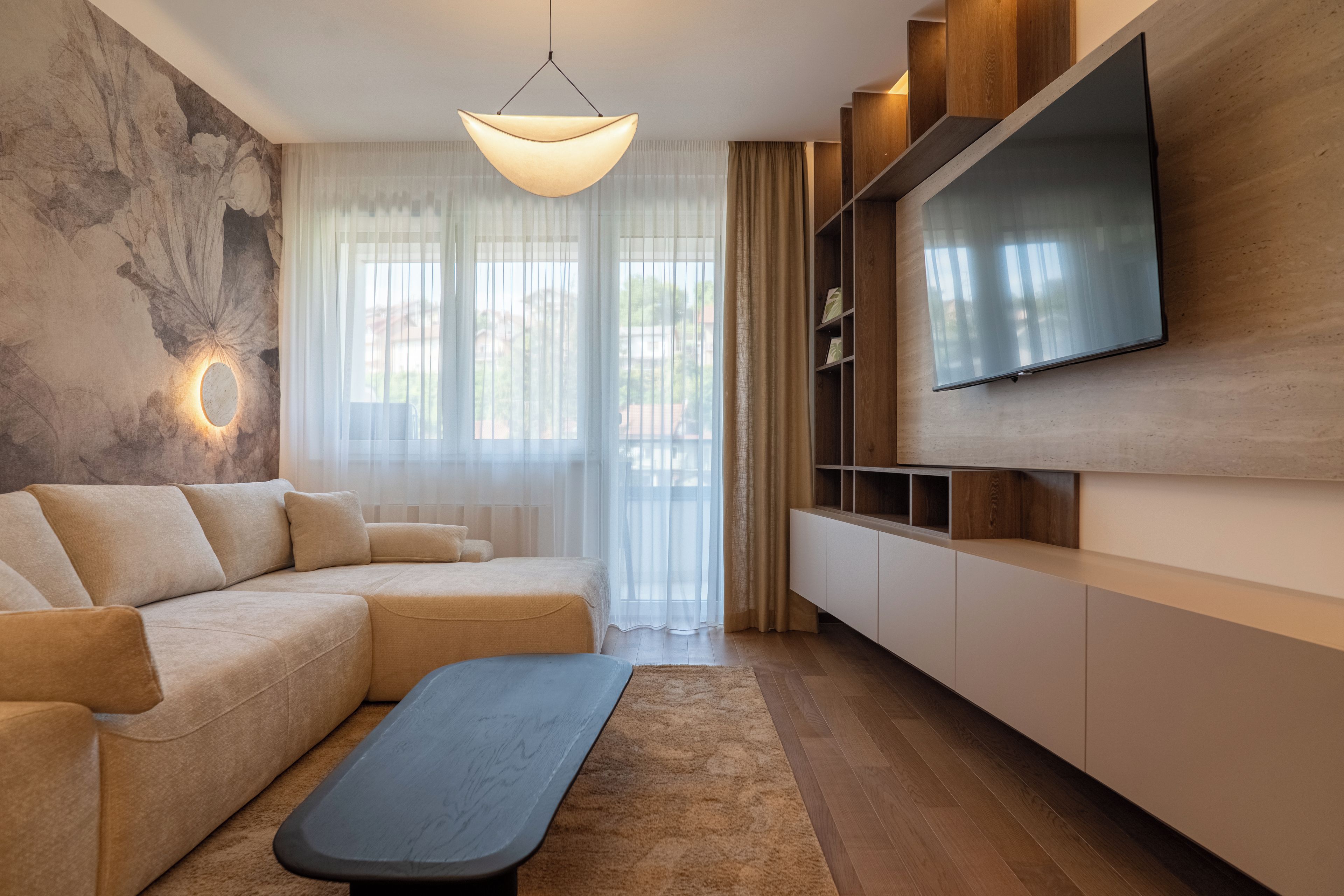 Un salon moderne avec un canapé d’angle, un téléviseur à écran plat fixé à un mur en bois et un luminaire suspendu.
