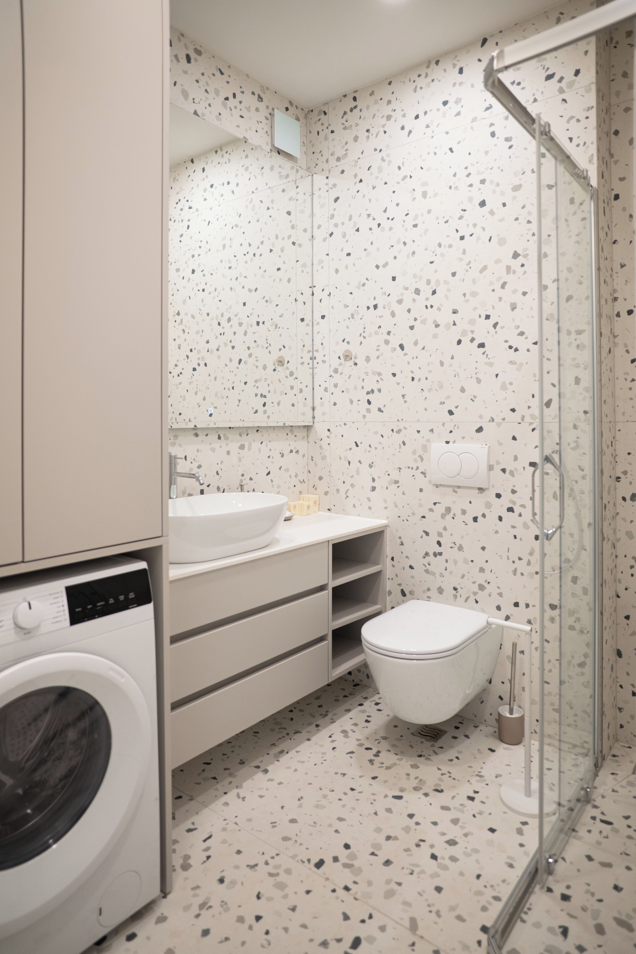 Ein modernes Badezimmer mit Waschmaschine, Waschbecken, Toilette und einer Duschkabine aus Glas.