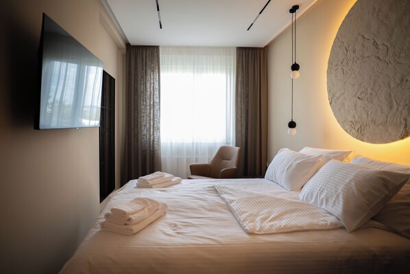 A hotel room with a bed, a chair, a TV mounted on the wall, and a large window with curtains. - Memory Residence Spa & Luxury Apartments (Banja Luka)