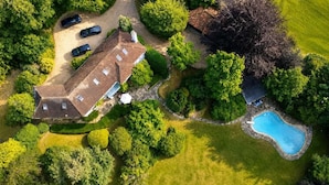 An aerial view of a property with a large house, a swimming pool, and several parked cars. - Brook House (Stoke Poges)