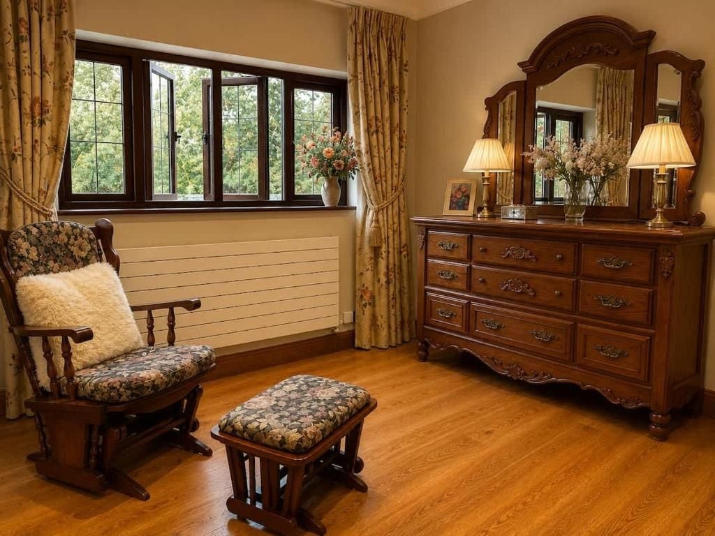Una habitación con una silla y un banco de madera, un aparador con cajones, un espejo y una ventana con cortinas.