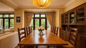 A dining room with a wooden table, chairs, a vase of flowers, and a cabinet with glass doors. - Brook House (Stoke Poges)