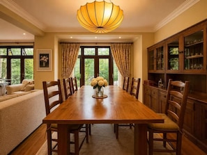 A dining room with a wooden table, chairs, a vase of flowers, and a cabinet with glass doors. - Brook House (Stoke Poges)