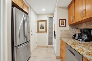 A kitchen with a stainless steel refrigerator, wooden cabinets, a granite countertop, and a coffee maker. - Oceanfront Resort on N. Kaanapali Beach | Pools | Dining | Free Trolley (Lahaina)