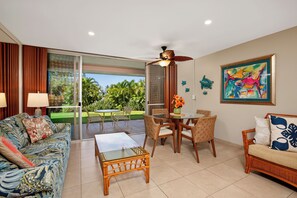 A spacious living area with a glass sliding door leading to a balcony, a dining table with chairs, a sofa, and a ceiling fan. - Oceanfront Resort on N. Kaanapali Beach | Pools | Dining | Free Trolley (Lahaina)