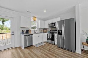 A modern kitchen with white cabinets, stainless steel appliances, and a wooden floor. - New 3BR Home- Less Than 1 Mile From The Beach (Gulfport)