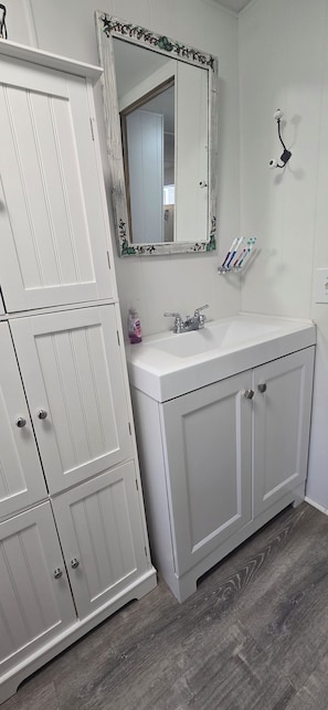 Une salle de bain avec un meuble-lavabo blanc, un miroir doté d’un cadre décoratif, un lavabo et un porte-brosse à dents.