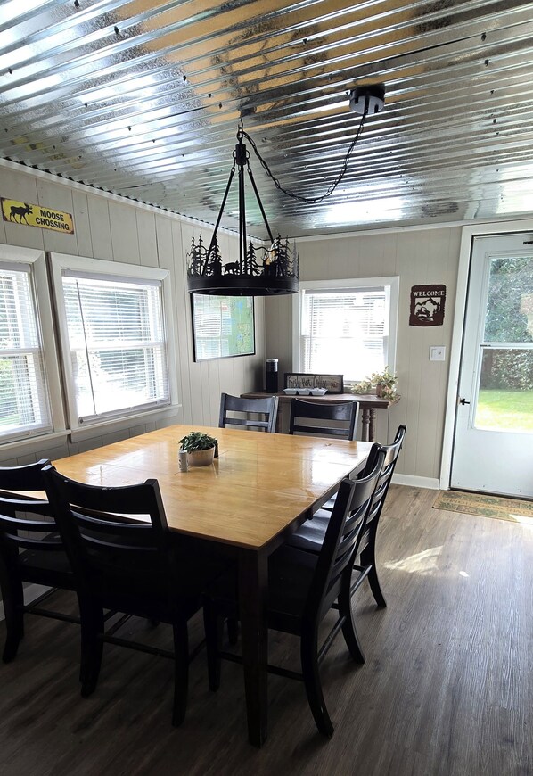 A dining area with a wooden table and chairs, a hanging light fixture, and a 'Welcome' sign.