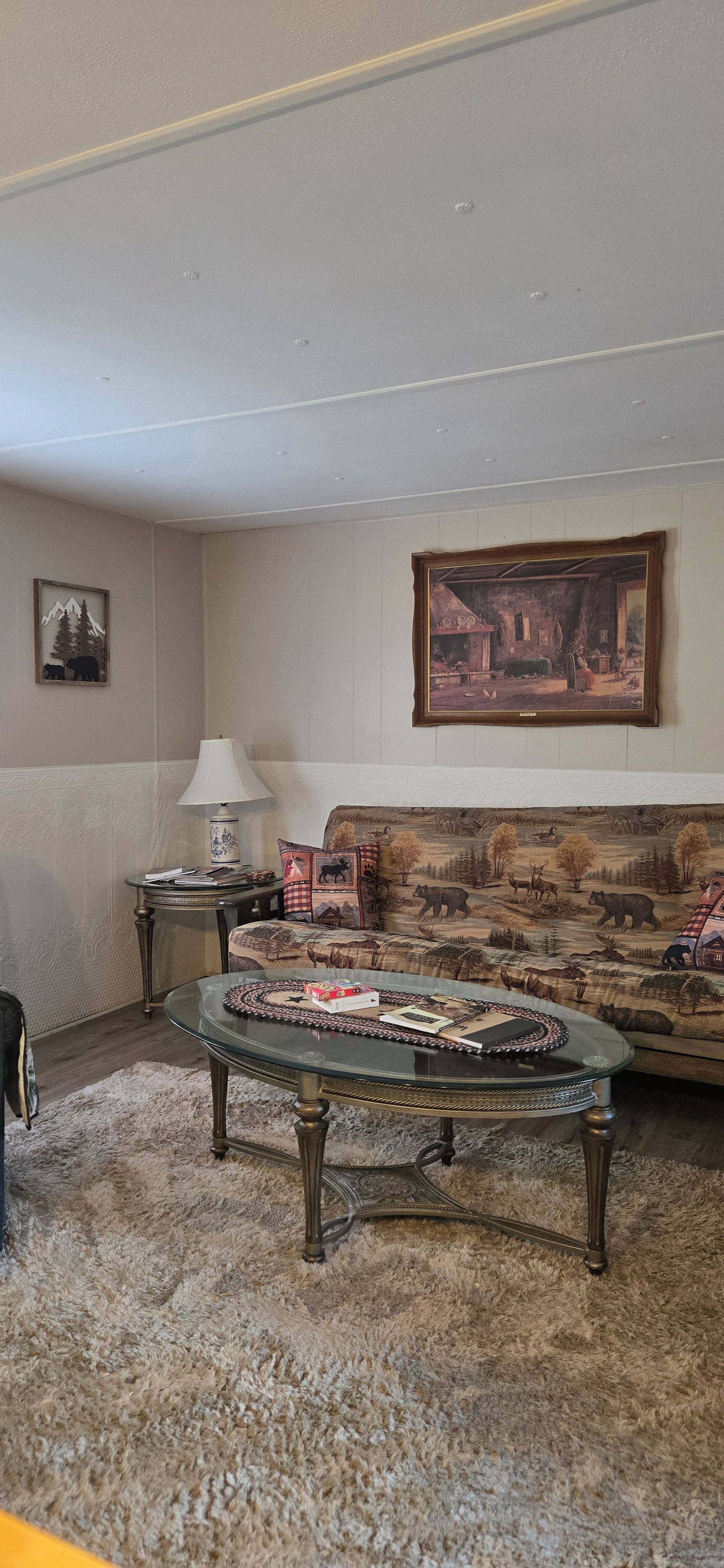 A living room with a sofa, a glass coffee table, a lamp, and a framed painting on the wall.