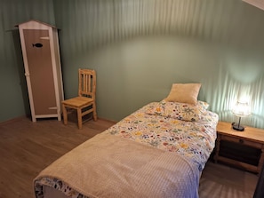 Quarto com uma cama, uma cadeira, um criado-mudo e um armário alto.