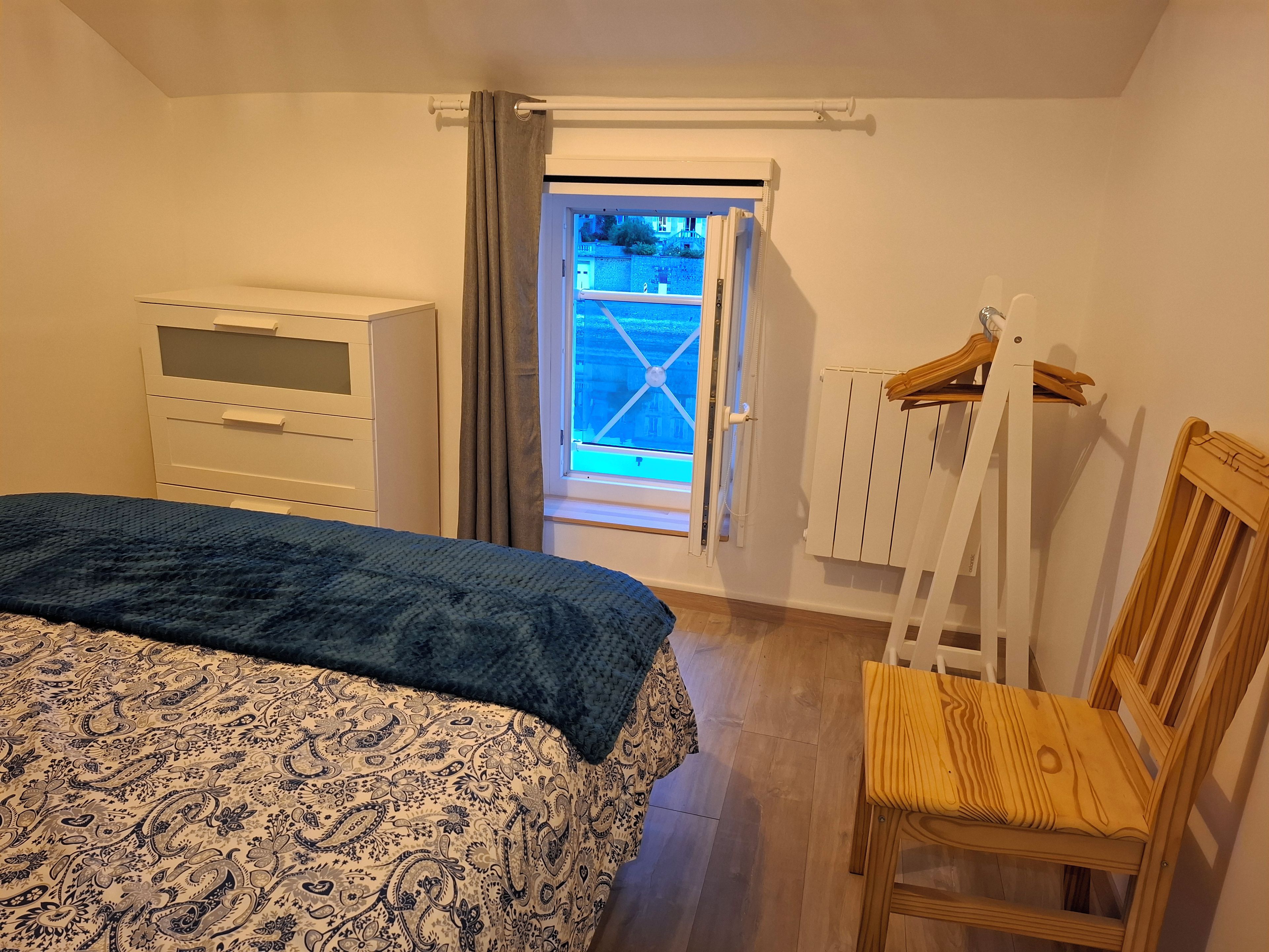 A bedroom with a bed, a chair, a wardrobe, and a window with curtains.