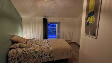 Un dormitorio con cama, lámpara colgante, ventana y una obra de arte en la pared.