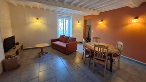 Una sala de estar con sofá, televisor, mesa de comedor con sillas y ventana.
