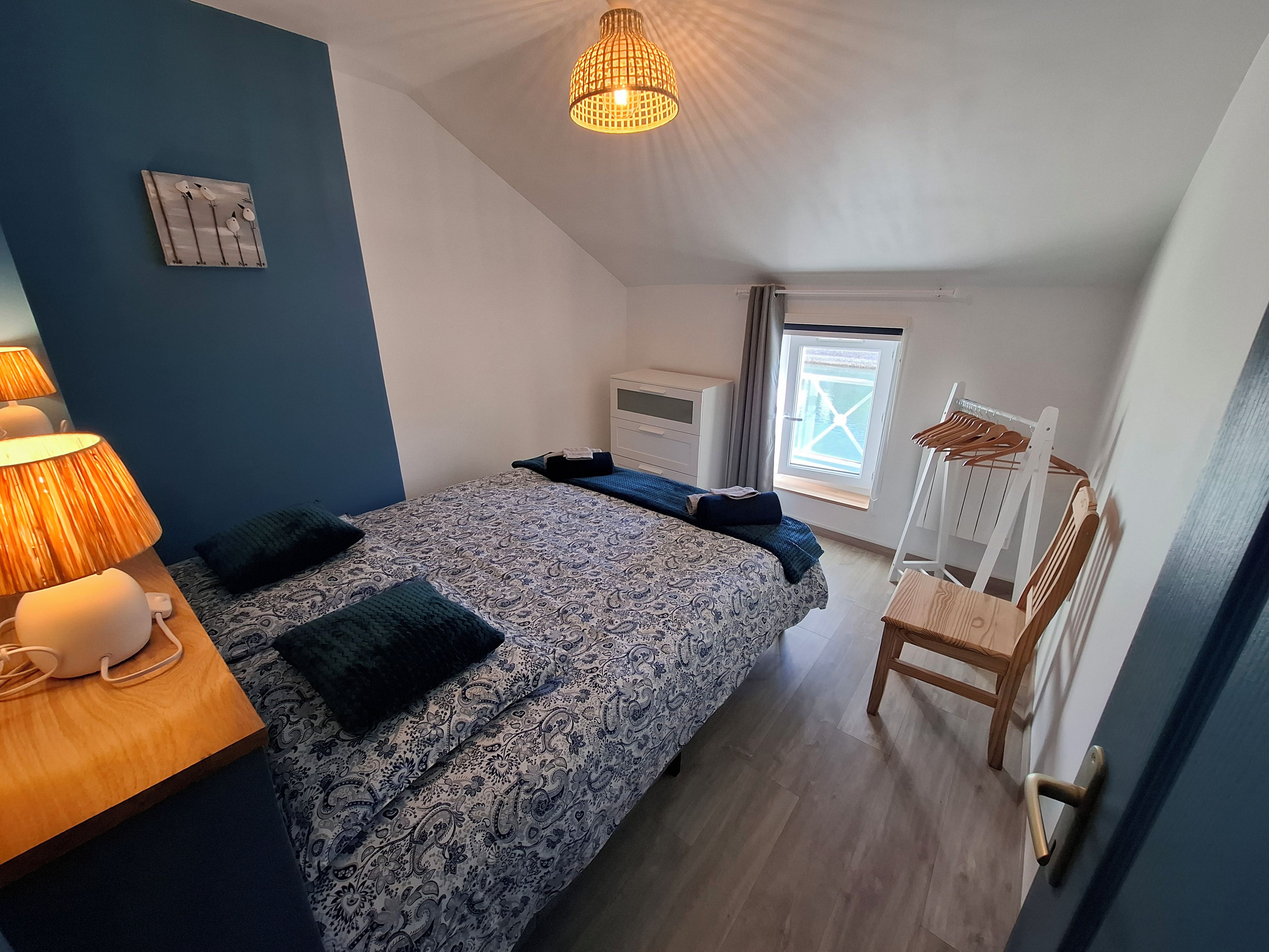 A bedroom with a bed, bedside lamps, a window, a radiator, and a chair.