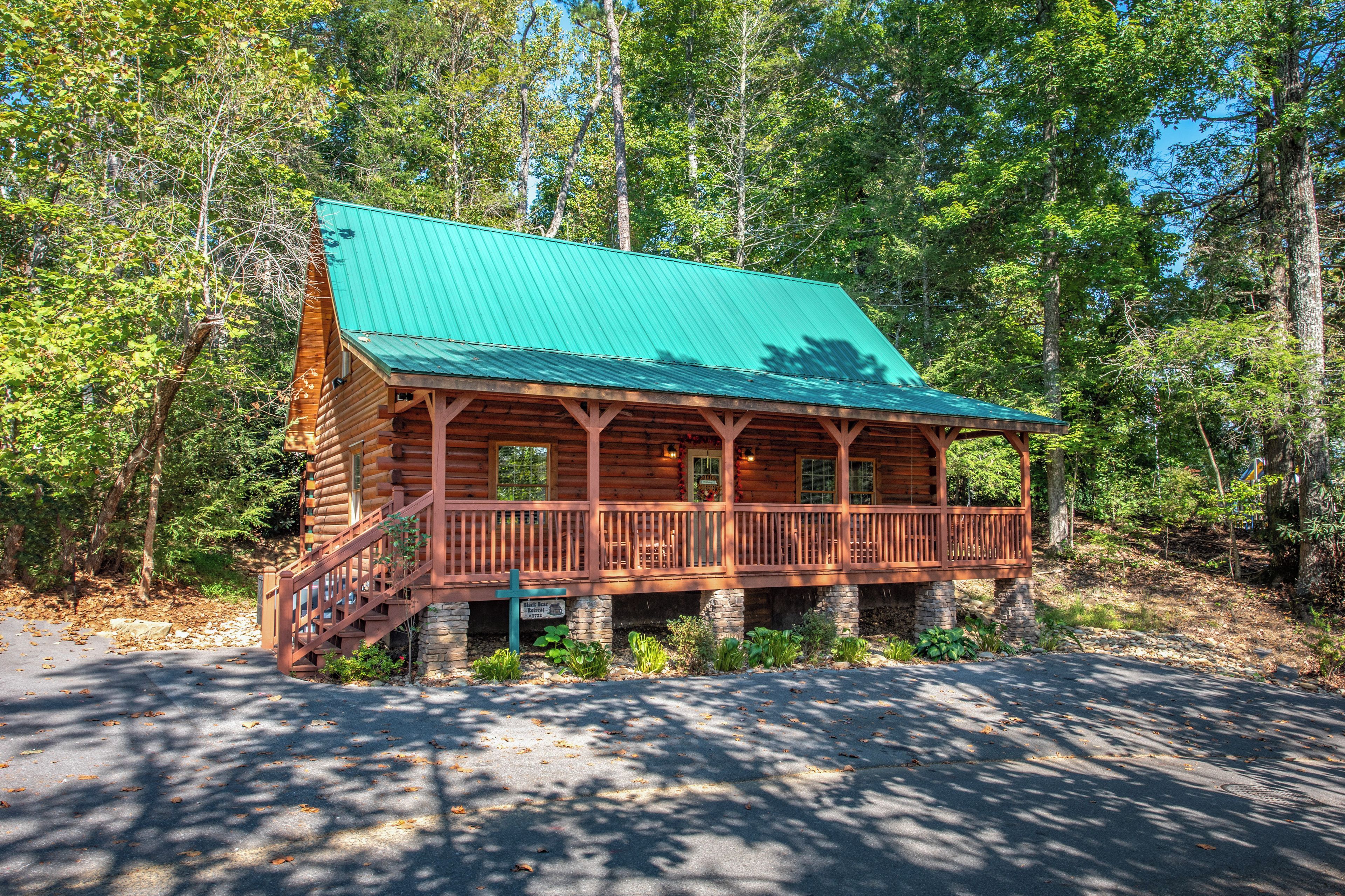 A log cabin with a green roof, a porch, and a stone foundation.