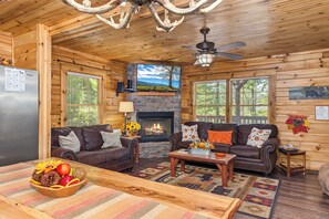 A log cabin interior with a fireplace, two sofas, a coffee table, and a dining table with a fruit bowl. - Welcome to Black Bear Retreat, your ideal Gatlinburg getaway nestled in the hear (Gatlinburg)
