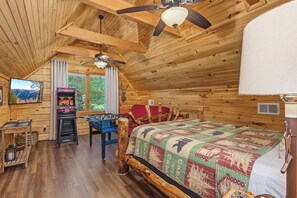 A cozy wooden cabin room with a bed, a foosball table, a television, and a ceiling fan. - Welcome to Black Bear Retreat, your ideal Gatlinburg getaway nestled in the hear (Gatlinburg)
